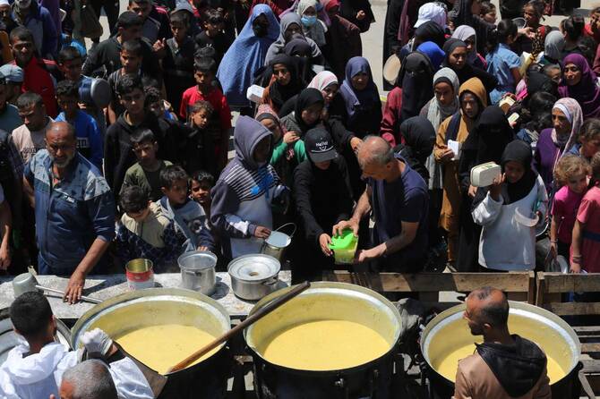 Palestinians queue for a portion of hot food distributed by a charity kitchen at the Nuseirat refugee camp in central Gaza Strip